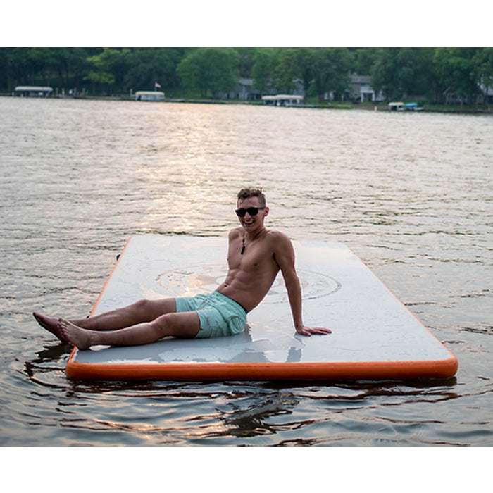 Paradise Pad 6'x10' Inflatable Water Mat in the middle of the water with a smiling person lounging on top.