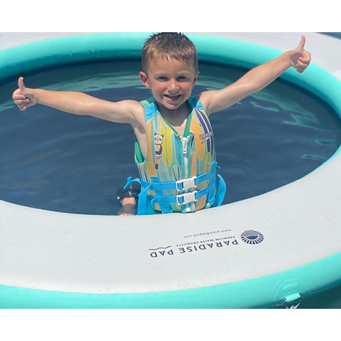 The Aqua variation of Paradise Pad 8ft Splash Island Water Mat with a child in the middle posing for a picture.