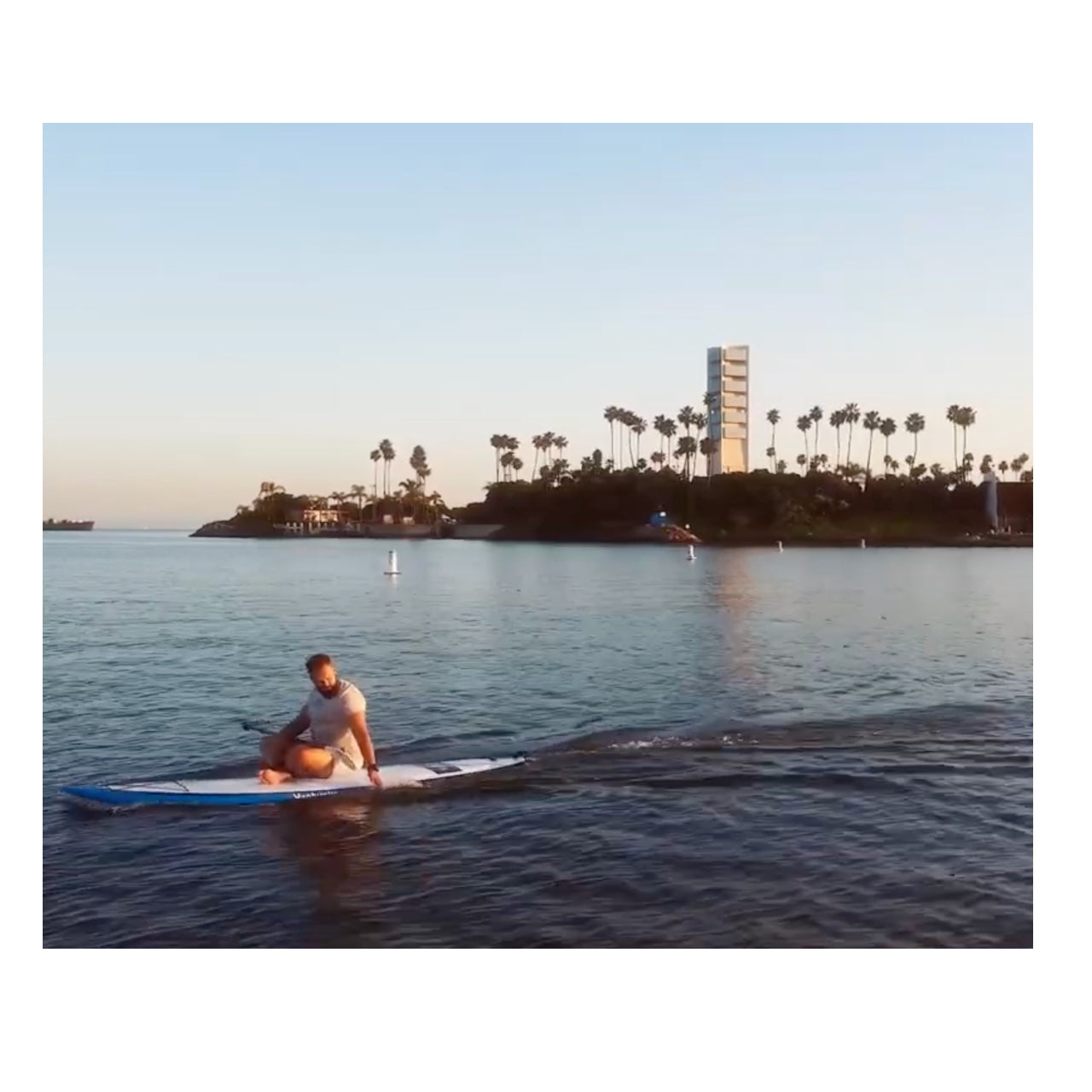 A young adult sits on his paddleboard on the water as the ScubaJet Pro Overwater Kit powers his paddleboard motor.